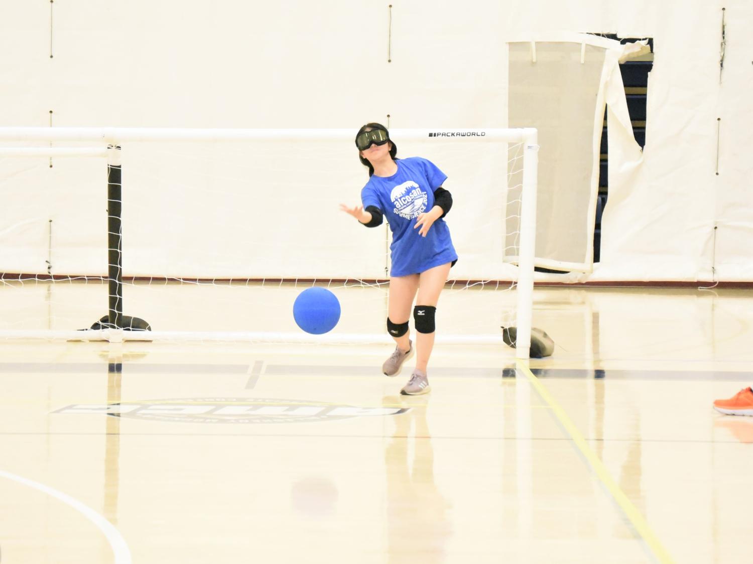 A blind player wearing ski goggles rolls a ball during a game of goalball.