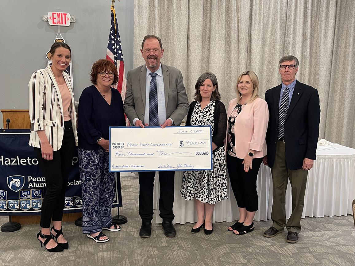 Six individuals standing in a row holding large check.