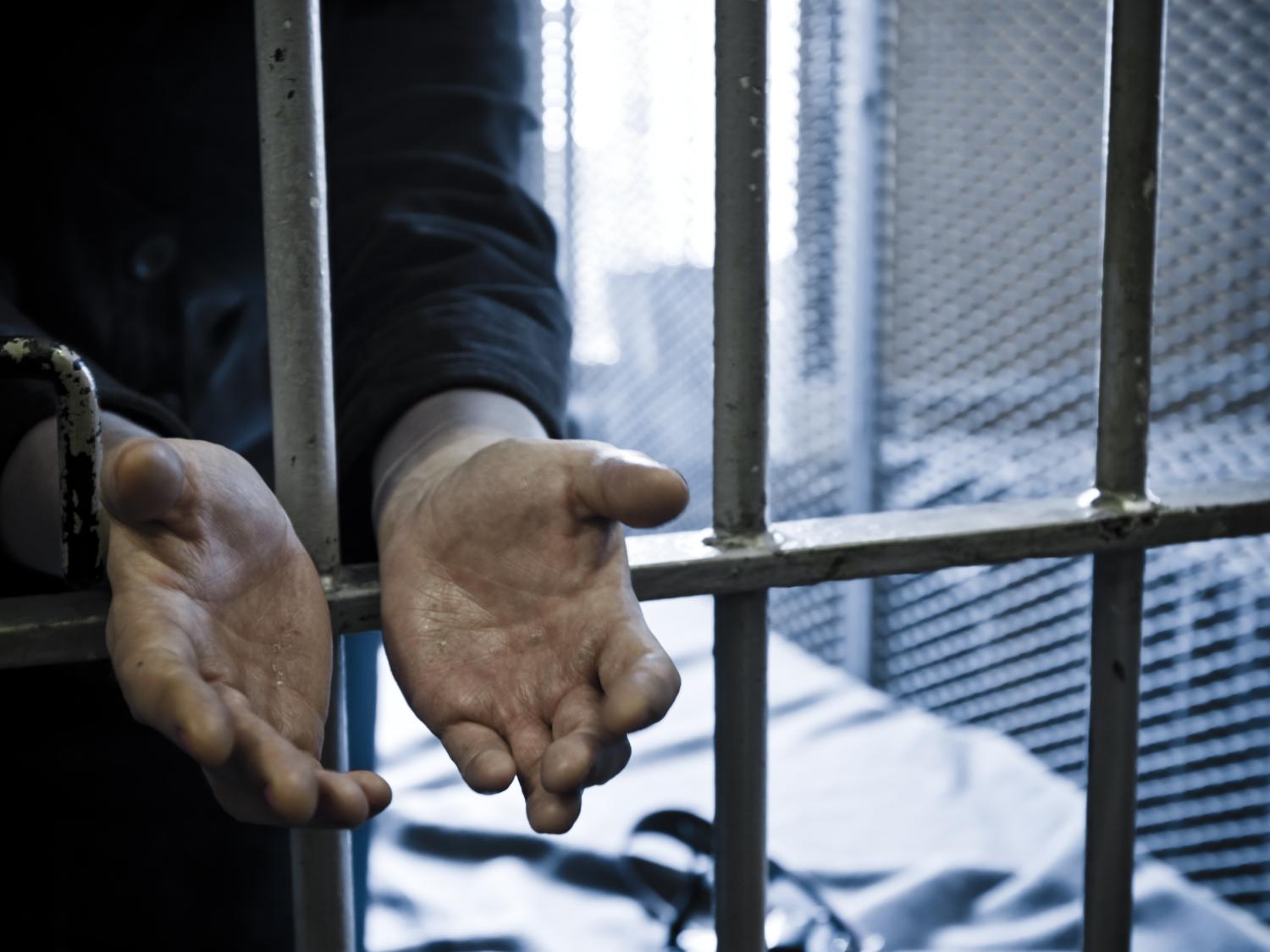 Handcuffed hands reaching out through a barred cell door