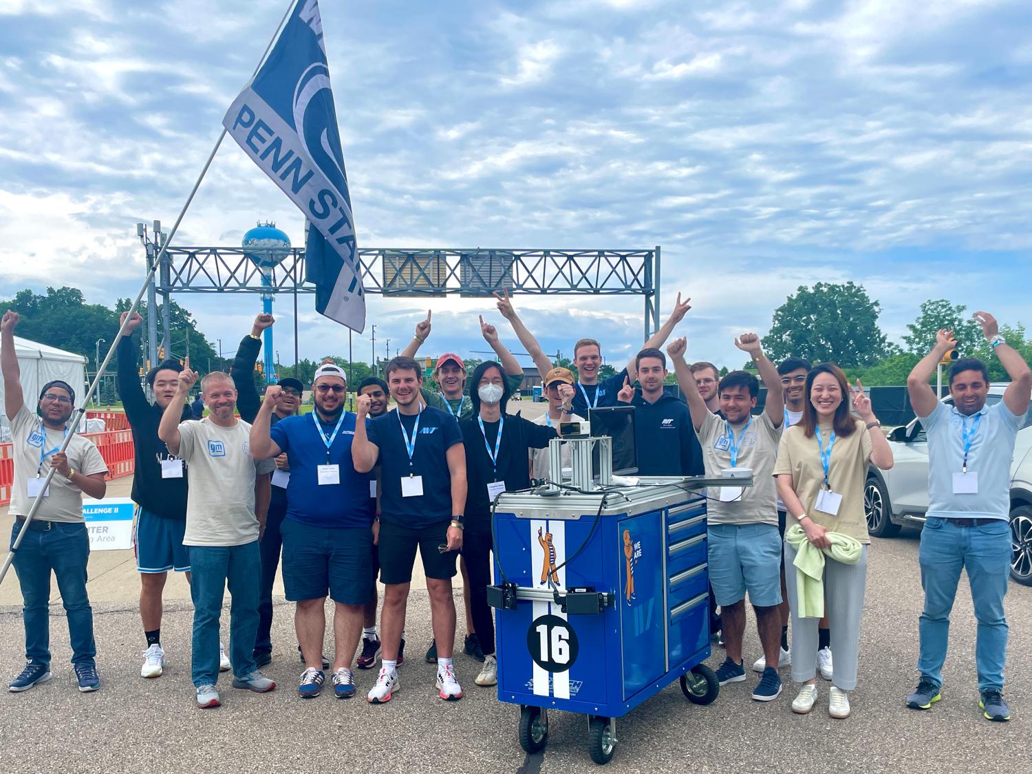 A blue cart is surrounded by several people cheering. Blue sky is visible in the background. 