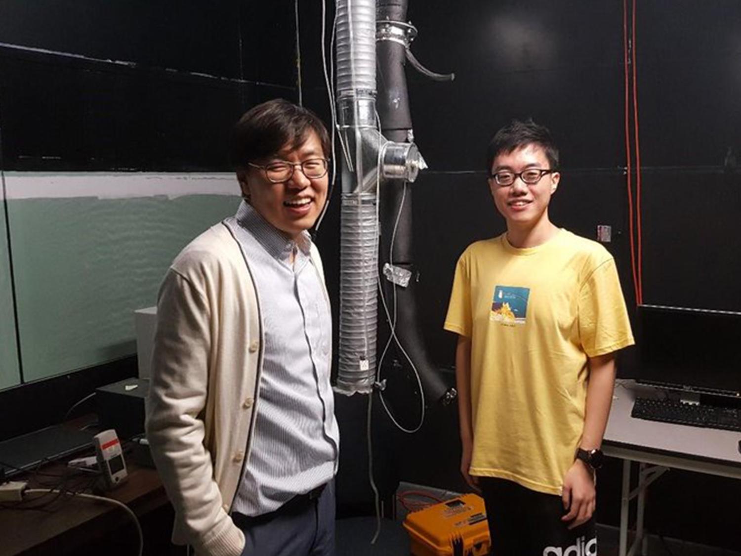 Two men wearing glasses pose near research laboratory equipment.