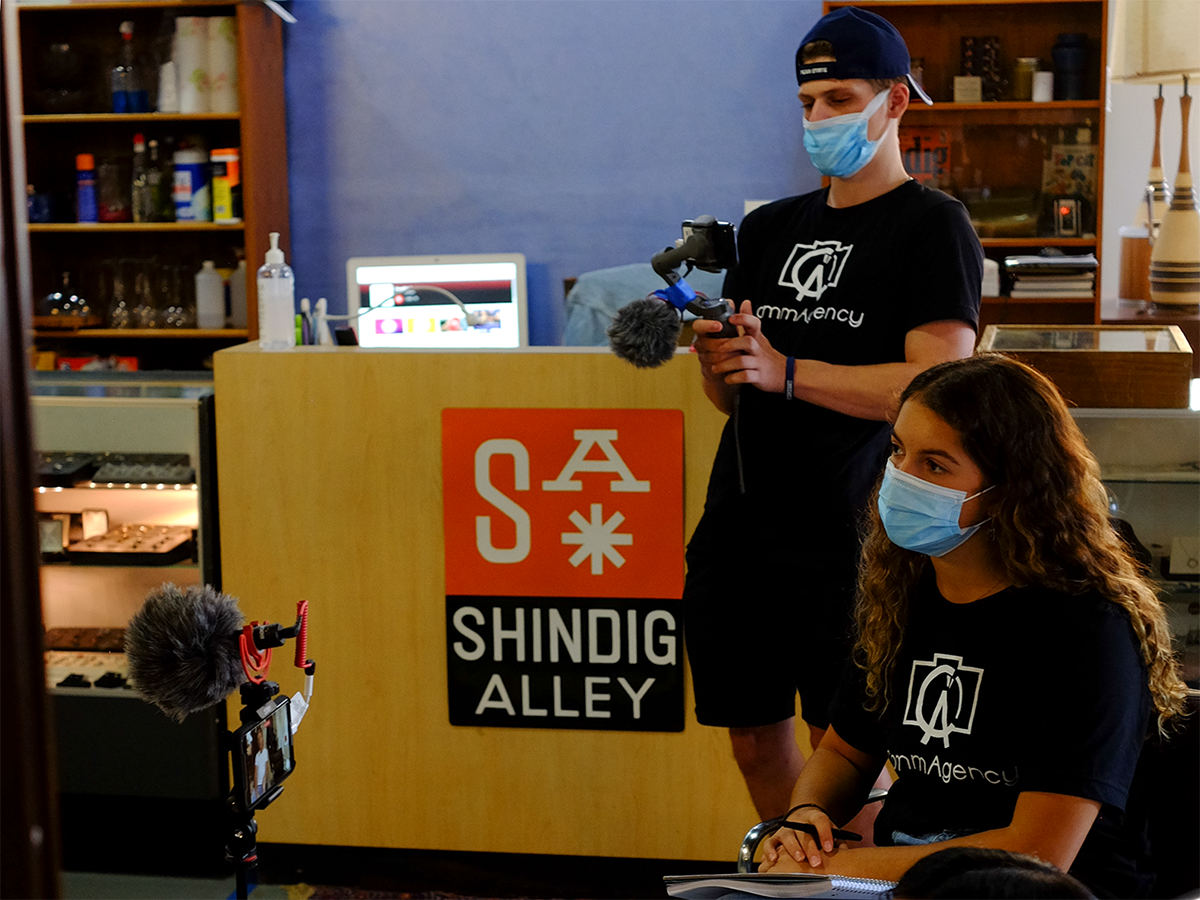 Two students in black CommAgency shirts record an interview. 