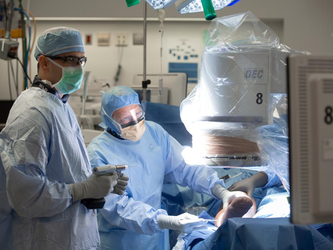 Two doctors in personal protective equipment stand next to an operating table with a patient on it.