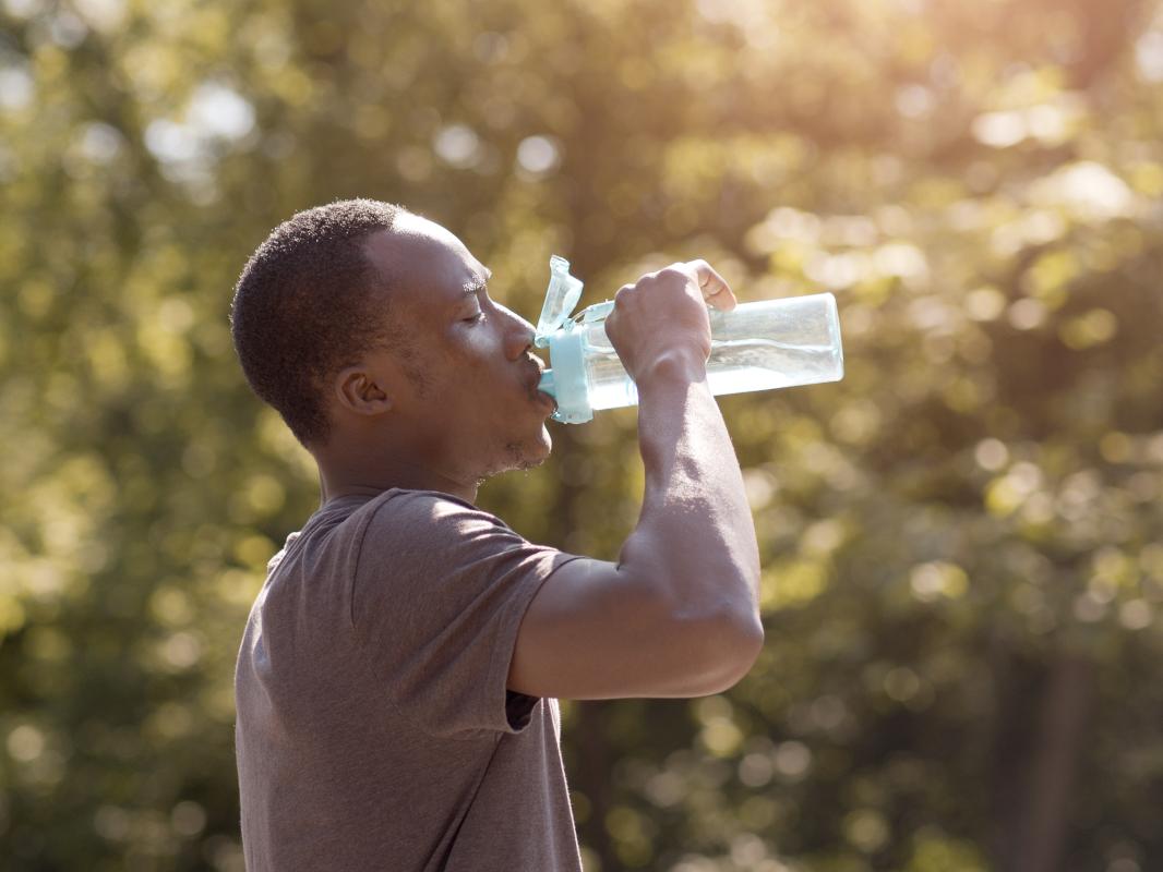A man drinks water from a bottle in a park.