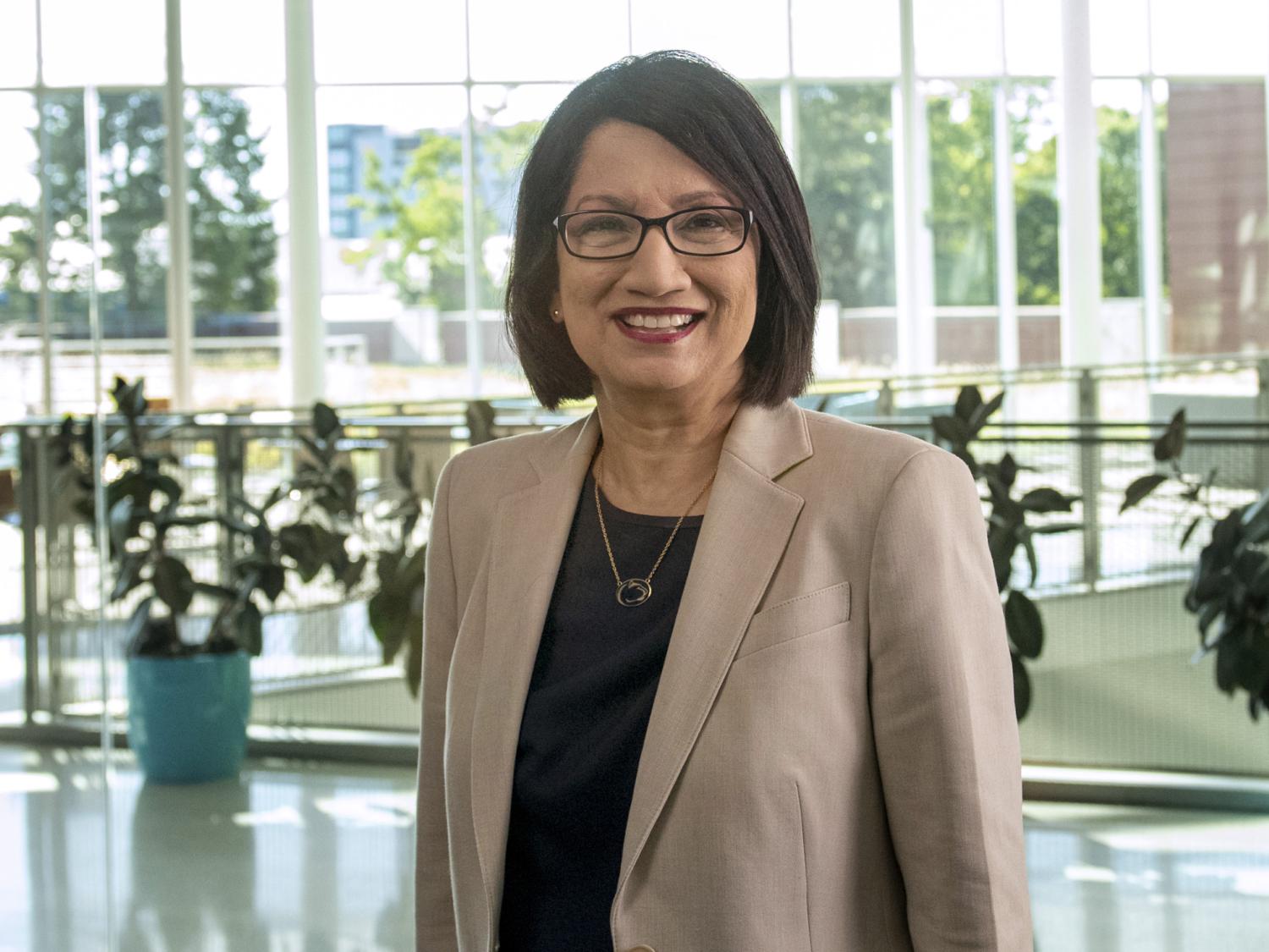 An image of Penn State President Neeli Bendapudi wearing a tan jacket while standing in a room filled with glass windows and sunlight