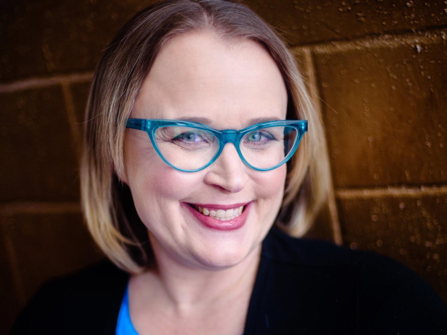 Portrait of woman wearing eyeglasses, a blue blouse and a black jacket.