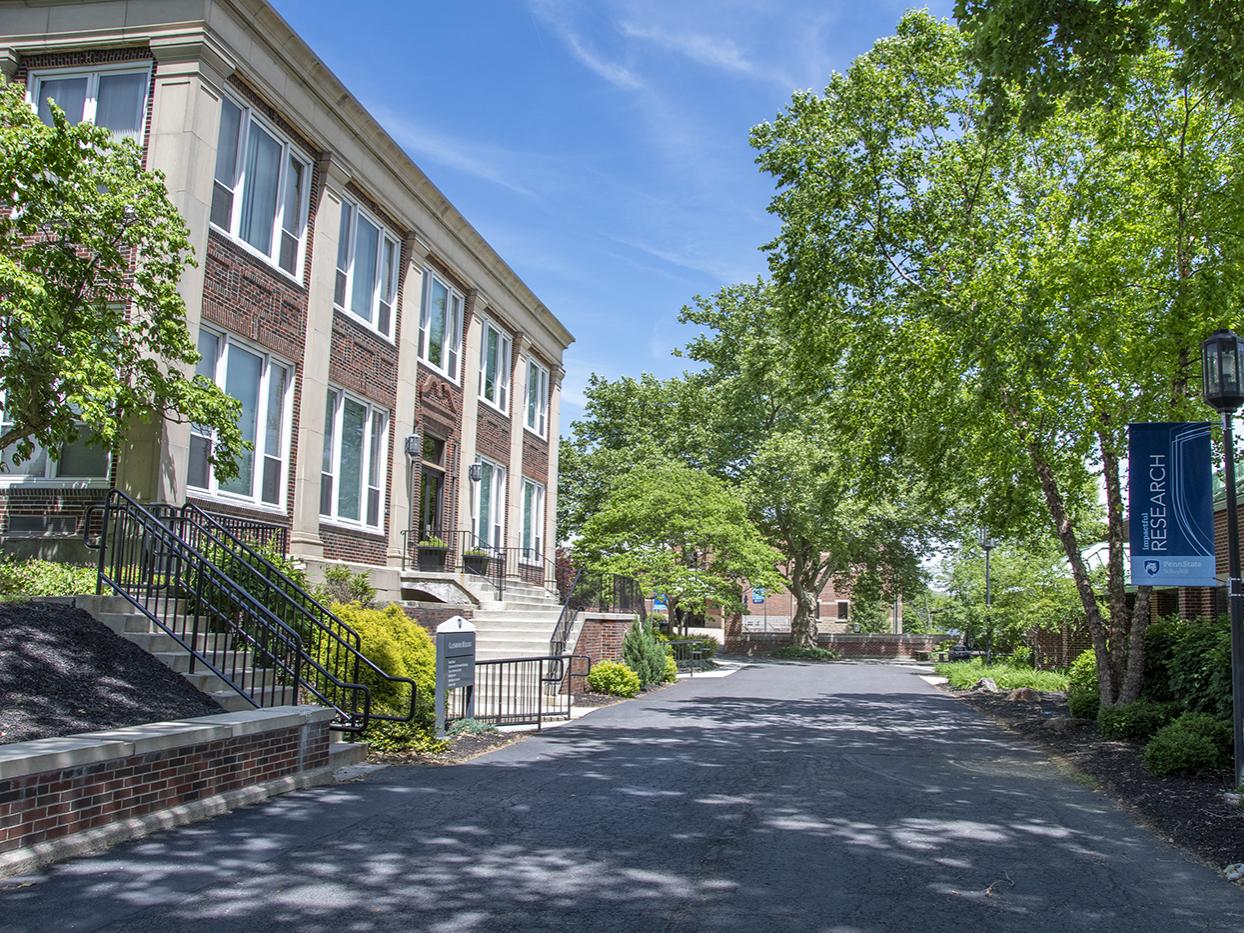 Two story brick building on left hand of photo with concrete pathway lined by trees