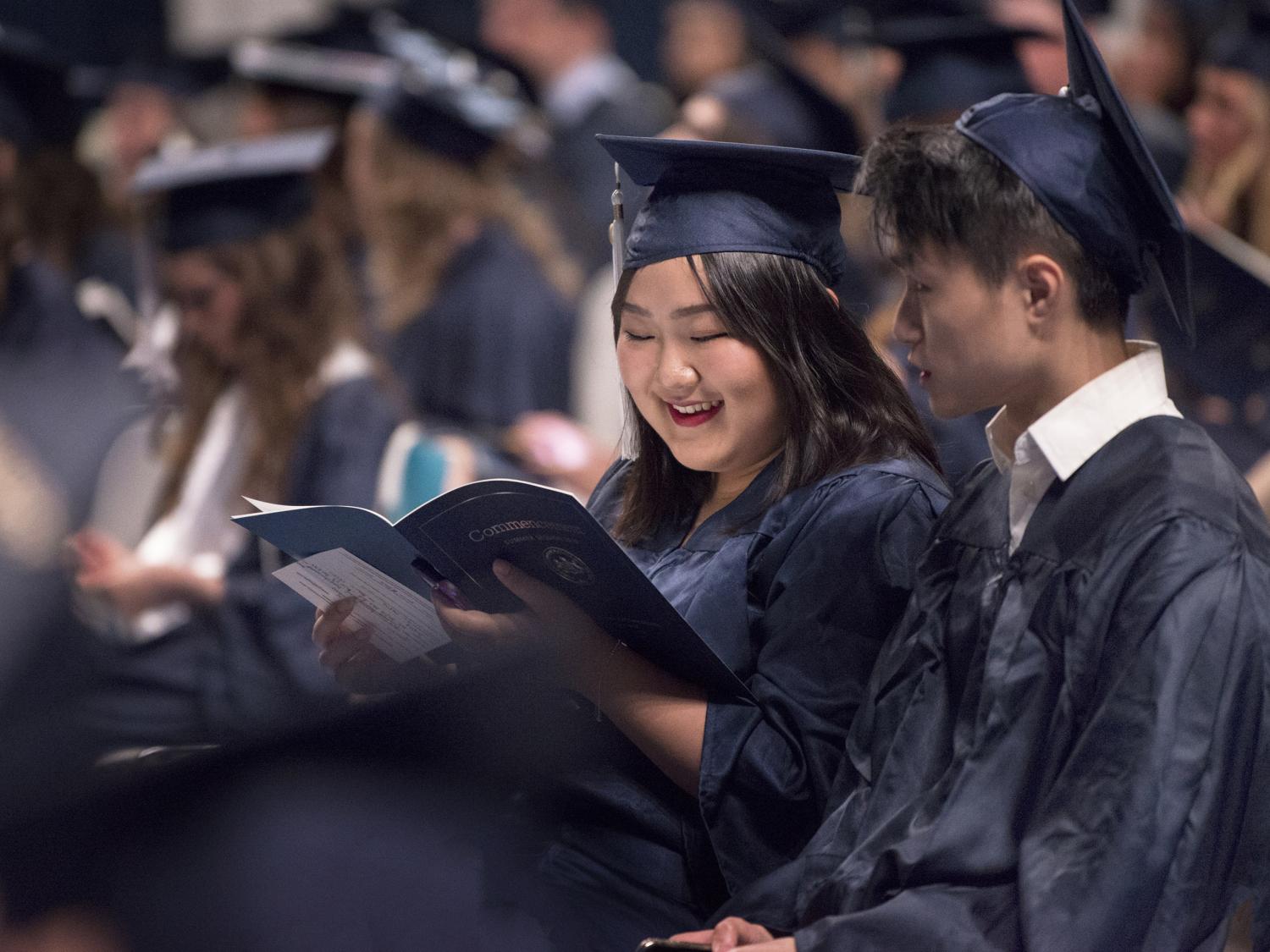 Two students wearing caps and gowns among the graduates at a commencement ceremony