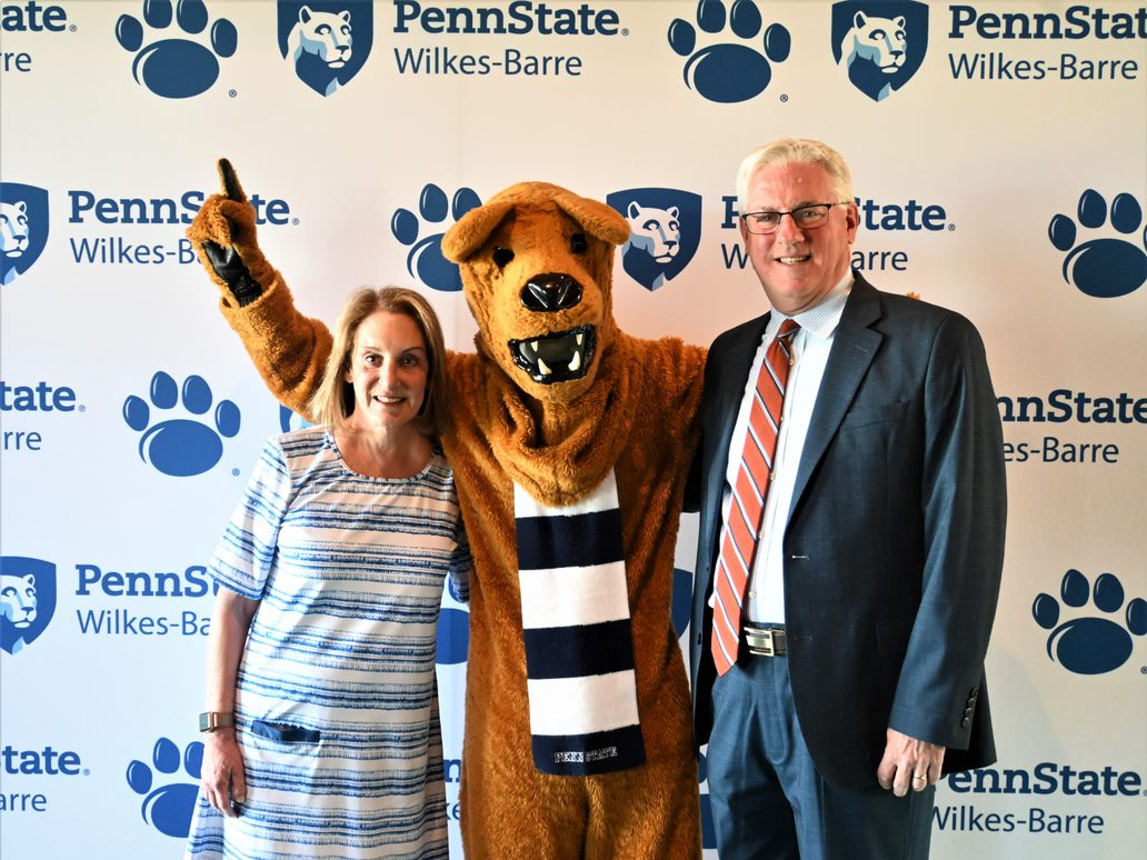 Two people standing with the Nittany Lion between them.
