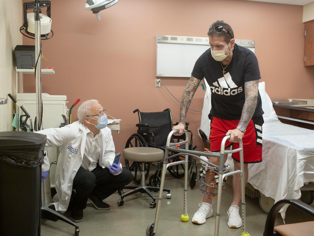 A doctor works with a patient that has a walker, and you can see an external device on the patient's leg that is used to correct bone deformities 