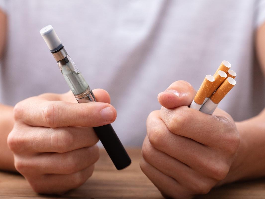 A man holds multiple cigarettes in his left hand and an electronic cigarette in his right hand. 