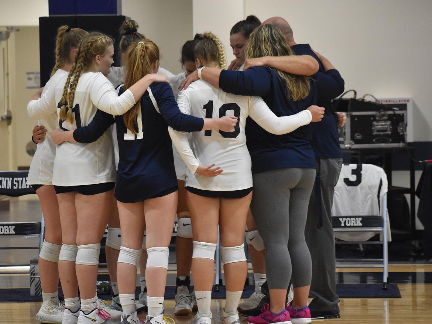 Women's volleyball players and coaches in a huddle on the basketball court