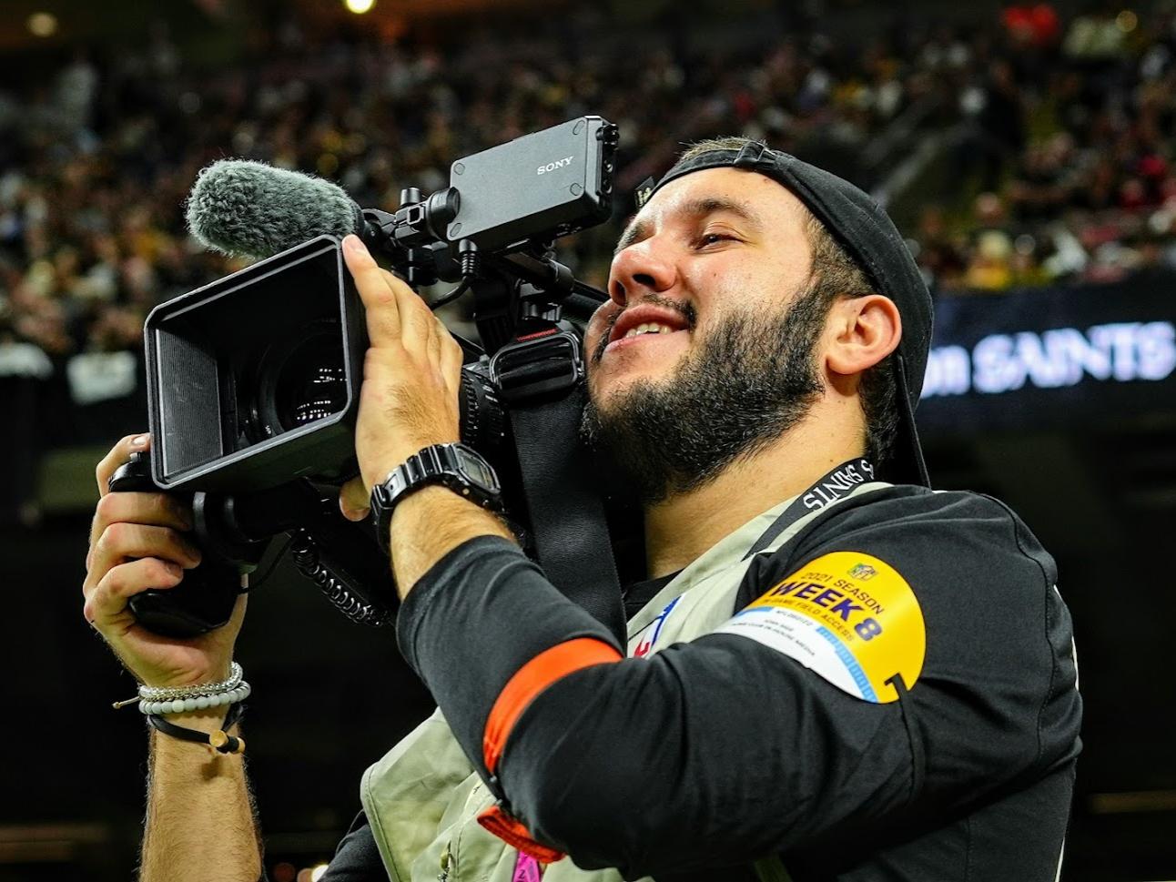 Josh Sige looks through a video camera on the sideline during an NFL game.