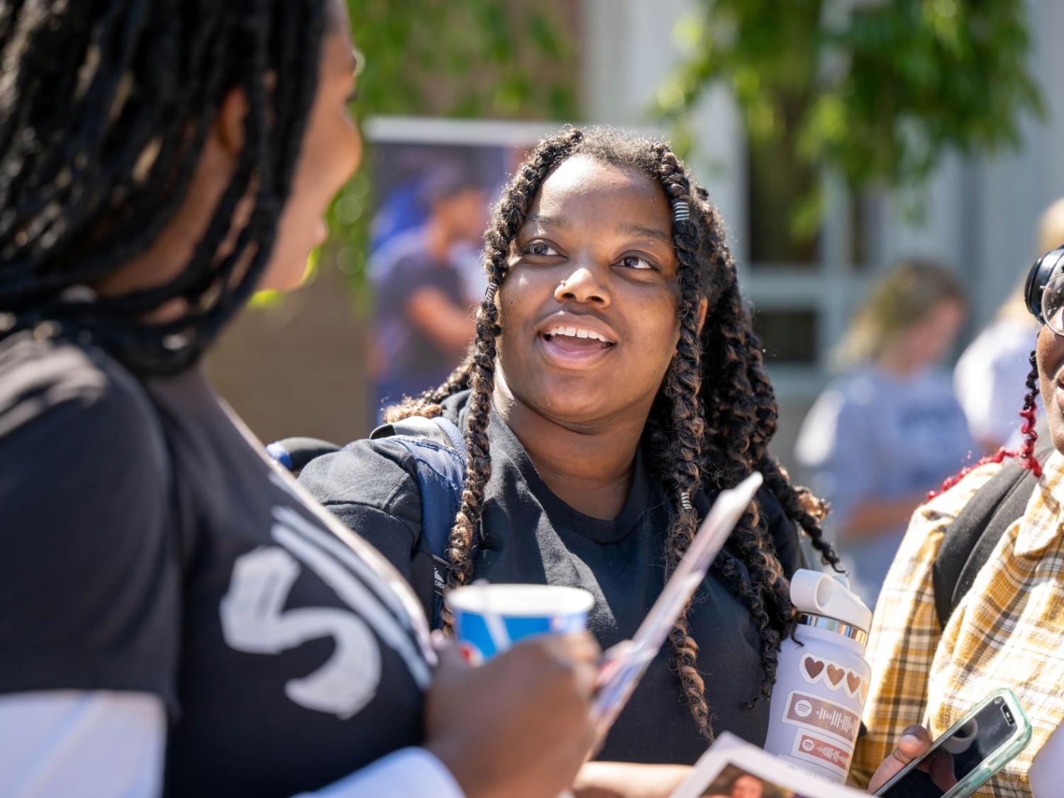 Three female students laugh while talking on the Reed Lawn during Penn State Behrend's Discovery Fair.
