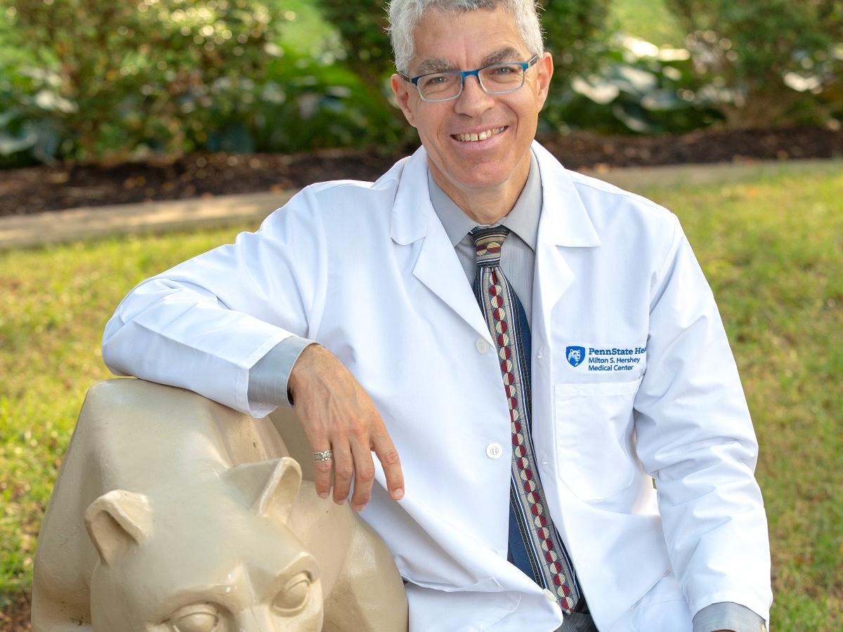 Dr. David Rabago sits near a statue of the nittany lion on Penn State College of Medicine's campus. 