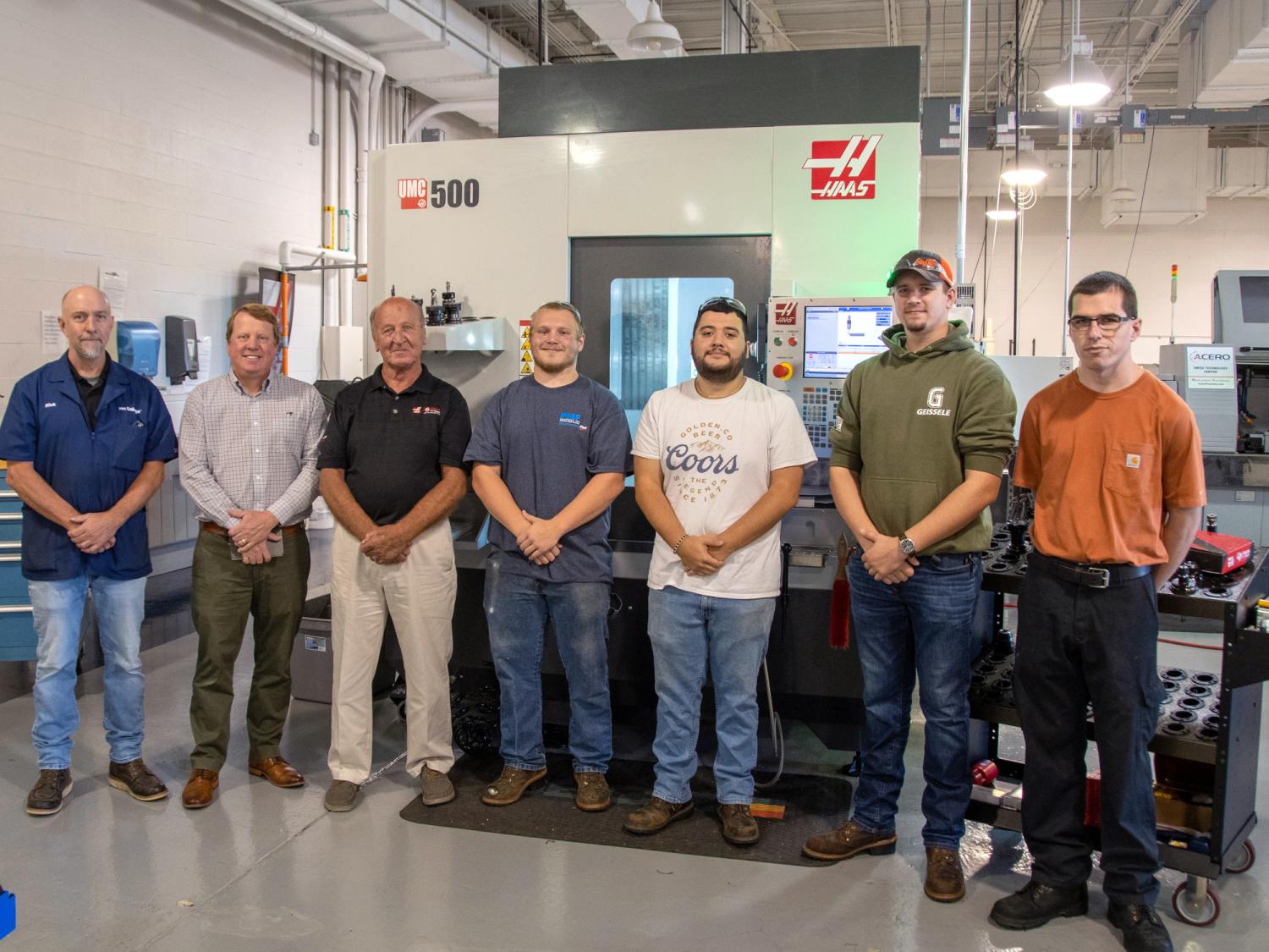 Students and representatives celebrate a donation of machinery in a factory.