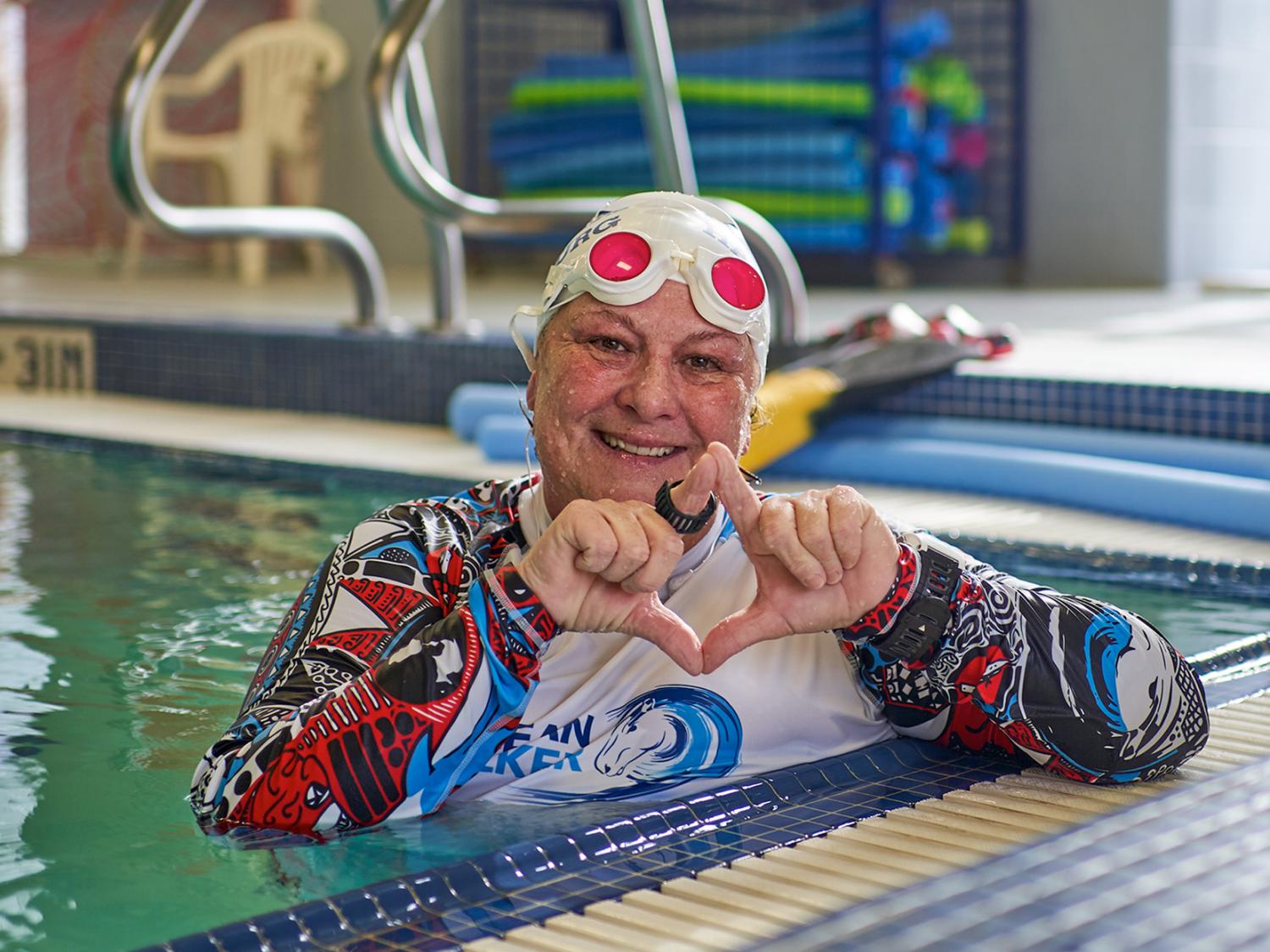 Holly Maitland-McKenna is shown in a swimming pool, smiling and making a diamond shape with her hands.
