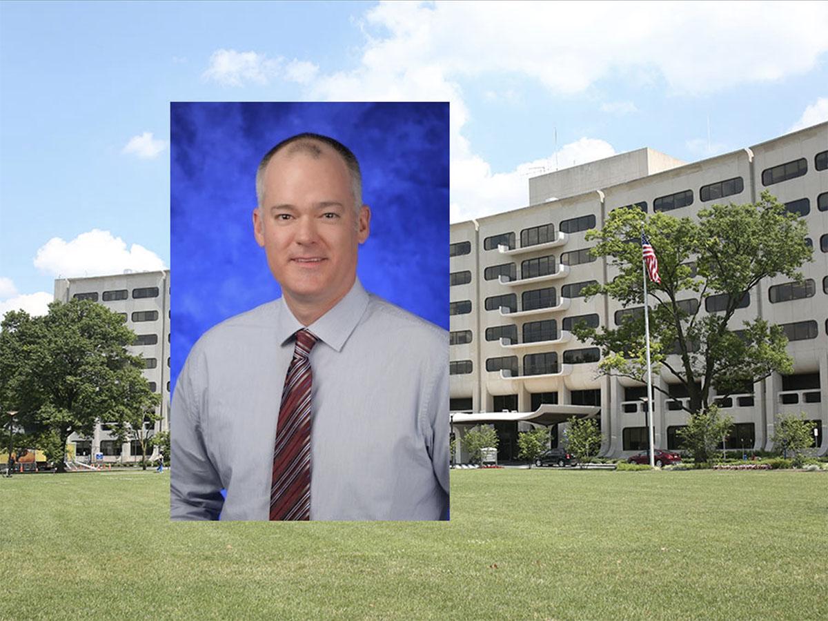 A head and shoulders professional portrait of Dr. Douglas Leslie against a background image of Penn State College of Medicine. 