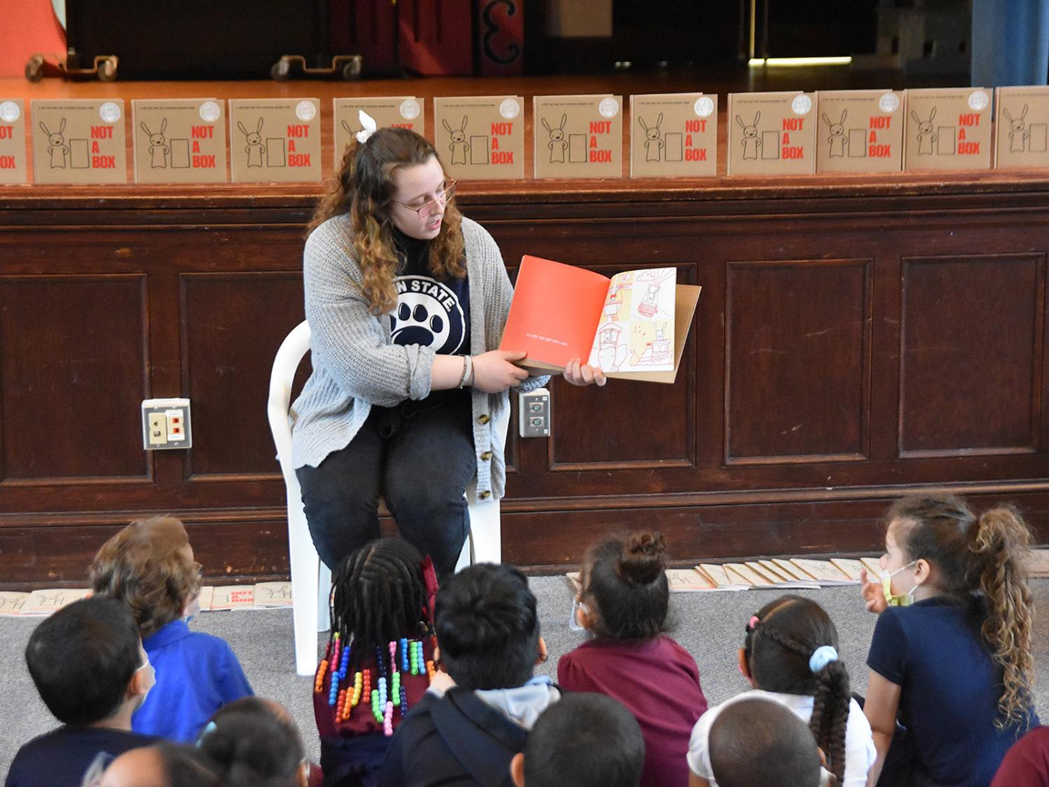 A Penn State York female student turns the pages of a book and reads to elementary school children.