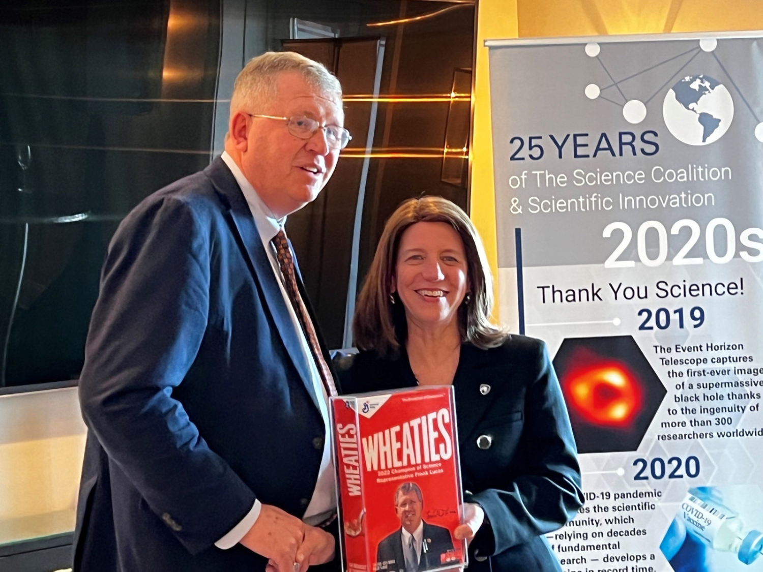 woman and man shaking hands while man holds Wheaties Box award
