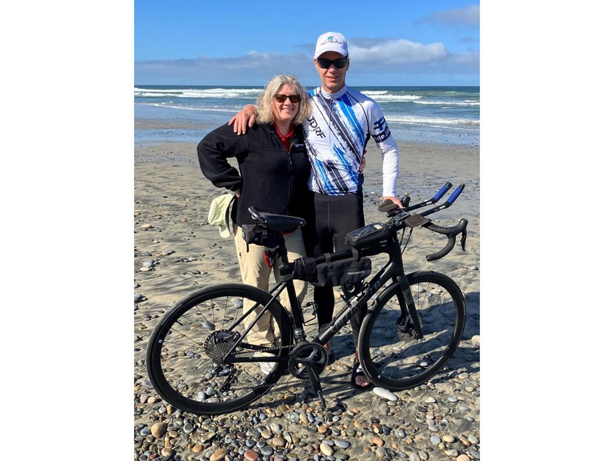 Randy and Tish Wussler pose at Torrey Pines State Beach in San Diego with a bike and the ocean in the background.