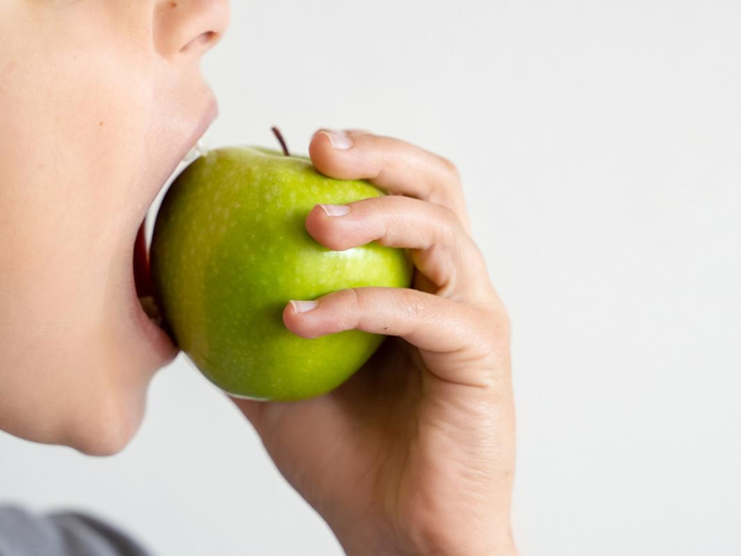 A close-up of a child biting into a green apple.