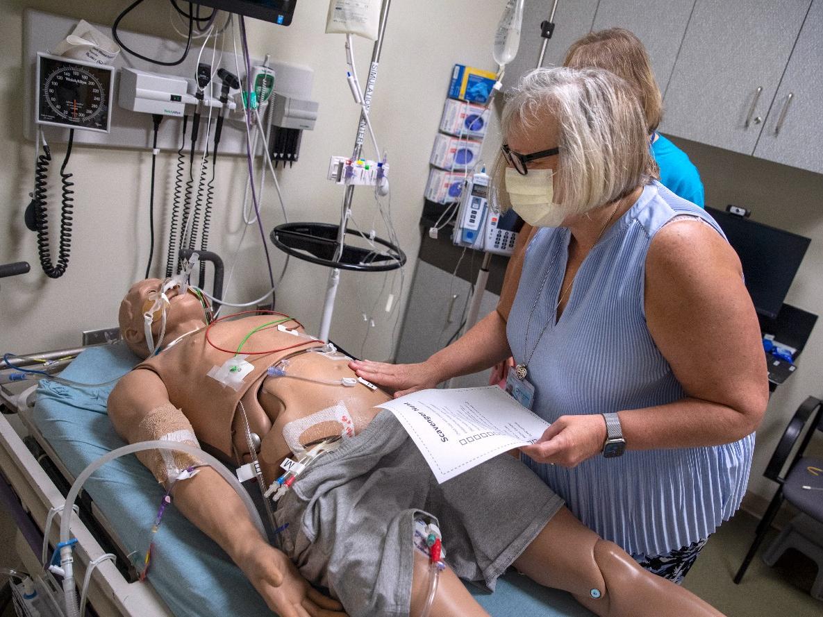 Dr. Susan Promes searches for various pieces of medical equipment on a mannikin in the Simulation Center.