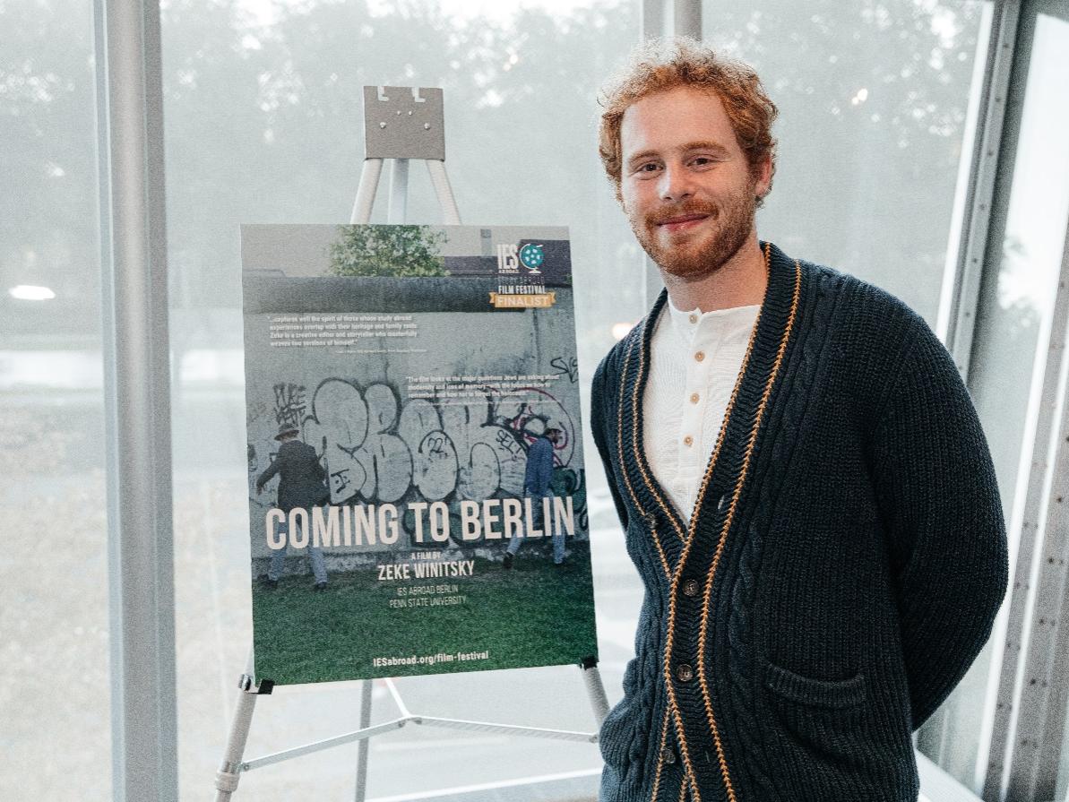 A man posing in front of a film poster for "Coming to Berlin"
