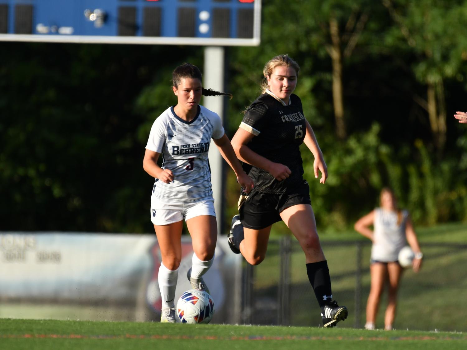 A Penn State Behrend soccer player advances the ball past her opponent.