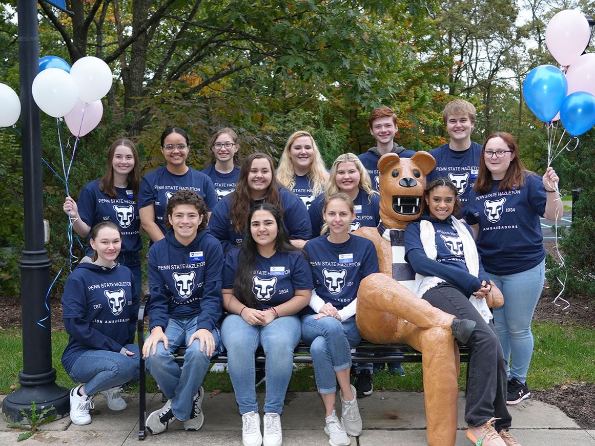 14 students seated in rows on a bench holding balloons.