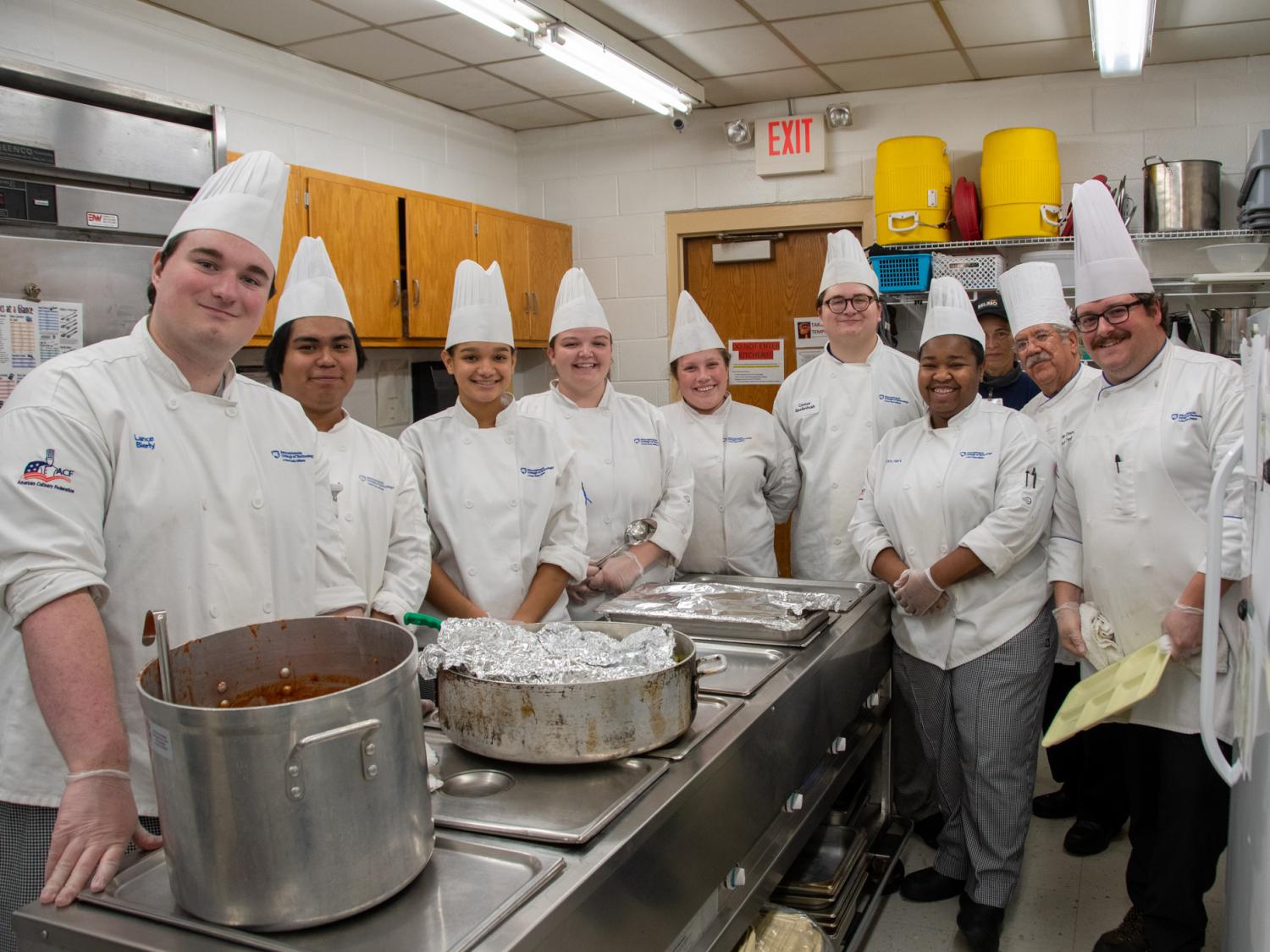 A group of Penn College students wearing chef's coats and hats standing in a kitchen