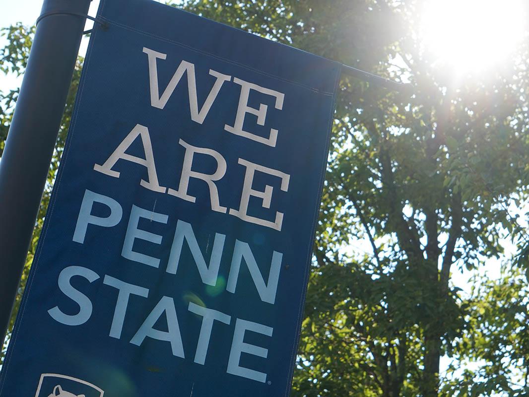 Blue 'We Are Penn State' banner with trees and sunshine in background