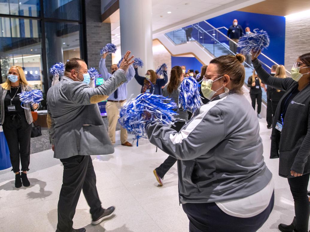 Staff members greet each other with pom poms in a hospital lobby