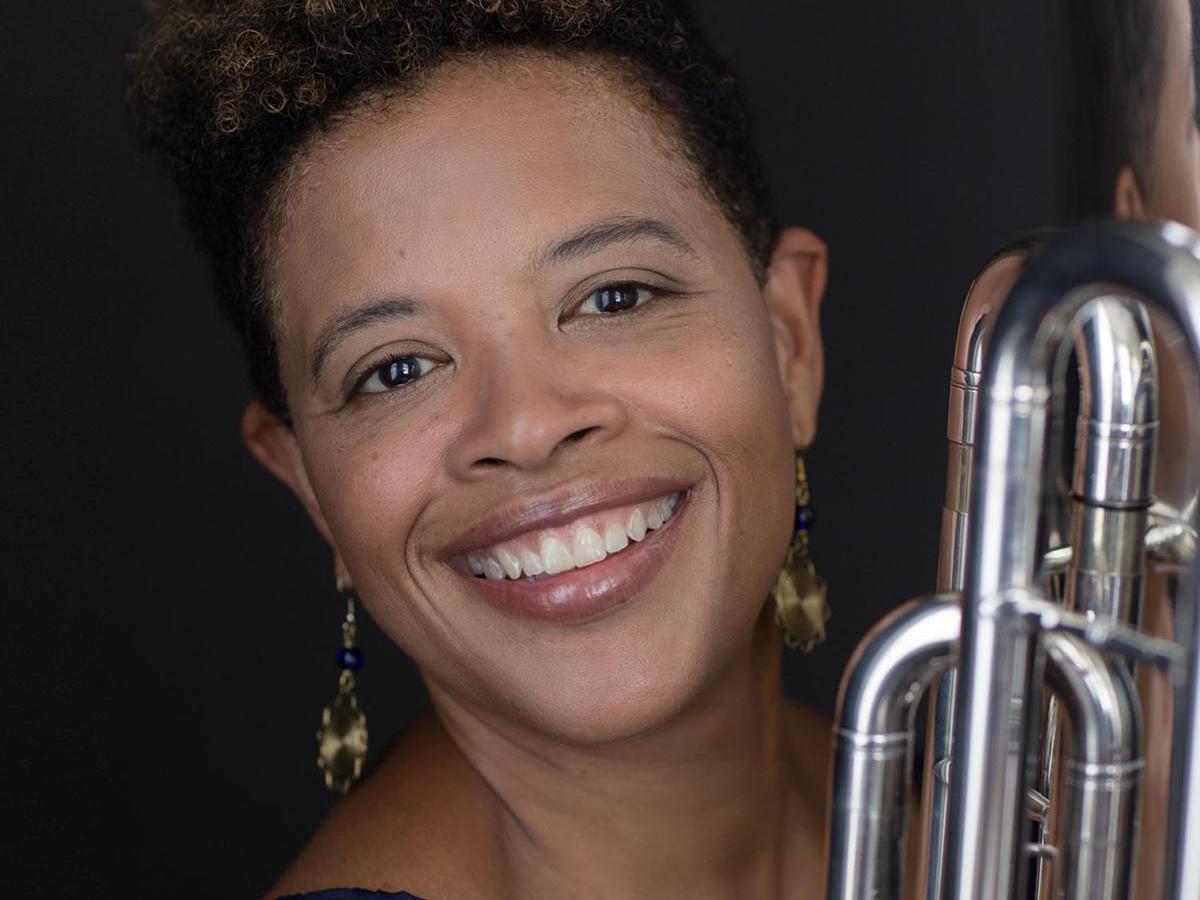 Woman with brown hair smiling and holding a tuba.