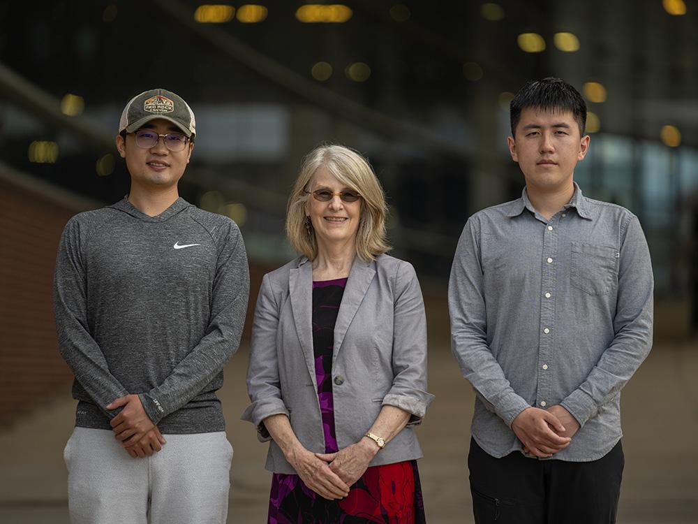 Three individuals pose outside a college building.