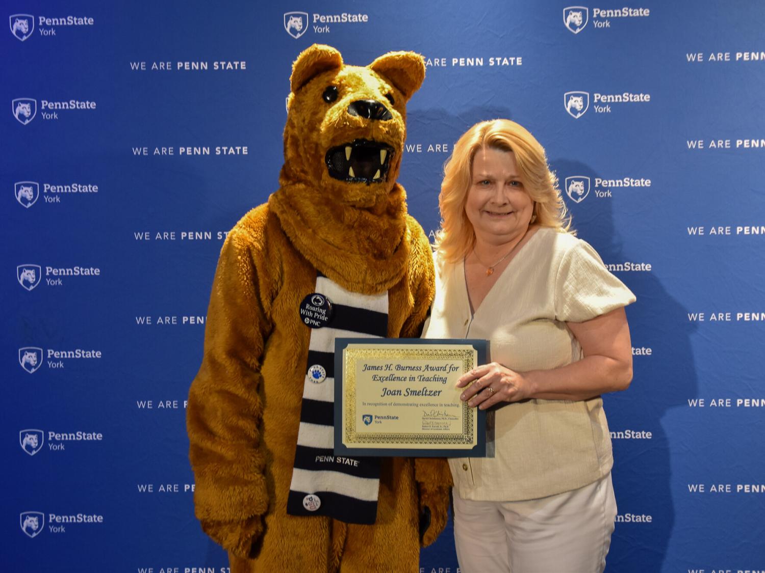 Nittany Lion costumed character presents awatd to female with long blonde hair
