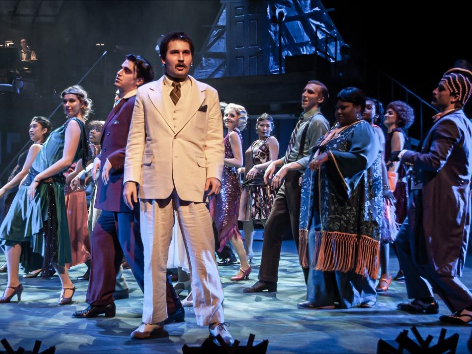 Musical theatre scene with man in white suit in spotlight