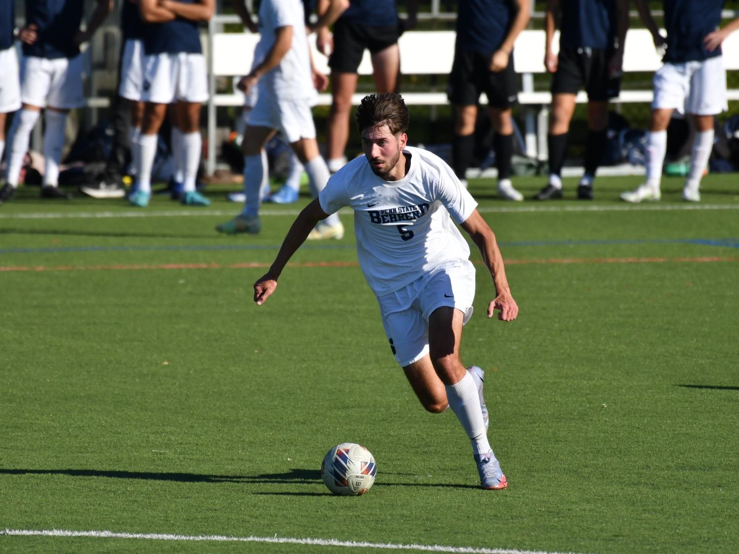 A Penn State Behrend men's soccer player advances the ball up midfield.