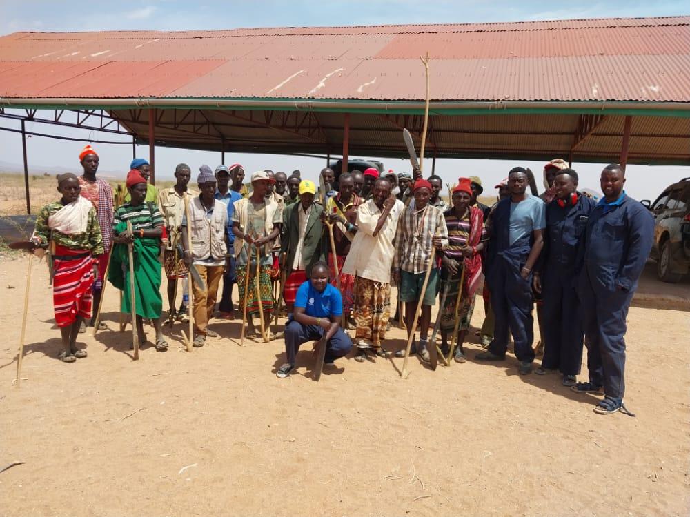 A group of pastoralists and Morans from Kor in Marsabit, Kenya who are being employed to remove weeds and improve the land through the application of biochar. Standing with PlantVillage Dream Team members from right (in blue overalls) Rashid Buroya, Fofen Lawrence, John Mayieka with Dream Team lead, Melodine Jeptoo in the front. 