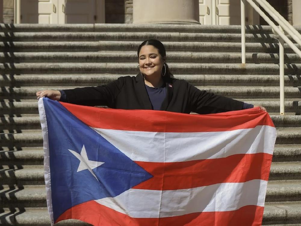 Zairi Mercader poses in front of Old Main holding the Puerto Rican flag.