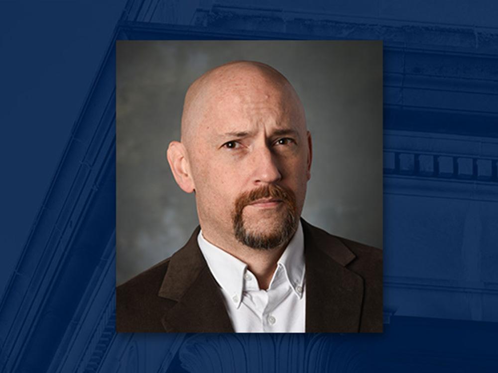 Head shot of bald man with goatee wearing brown sport jacket over white button-down shirt