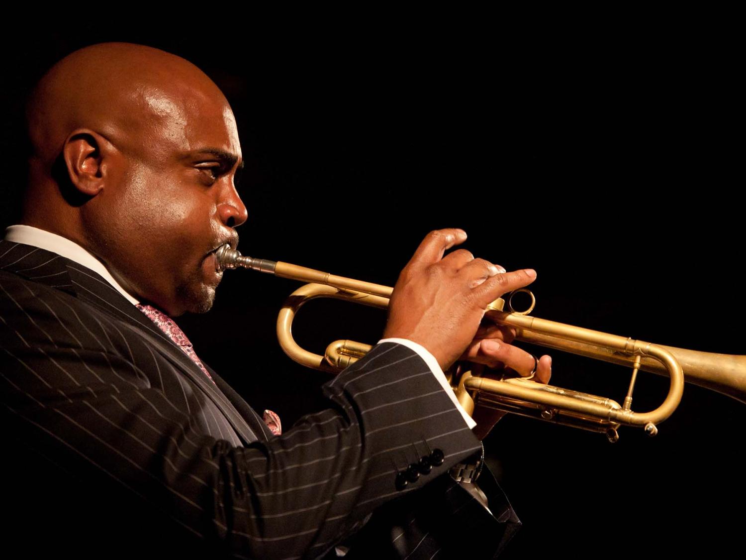 Side profile view of a man in a suit playing a gold trumpet.