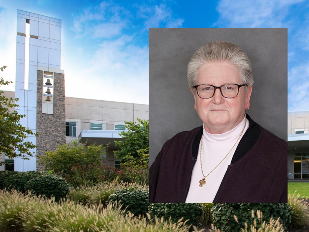 A photo of a woman with short hair and glasses sits on top of a photo of a hospital. Shrubbery and small trees are in the foreground of the hospital photo. A bell tower rises above the hospital on the left.