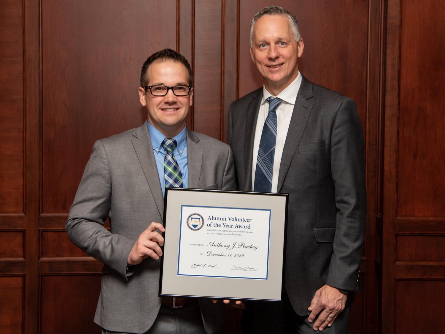 Anthony Peachy and Penn College President Michael Reed hold a certificate with a wood-paneled wall in the background