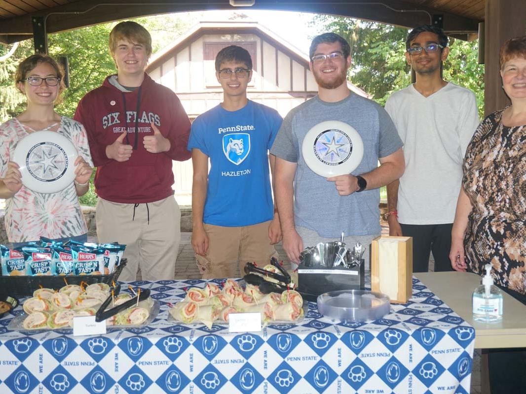 Students holding frisbees under an outdoor pavillion.