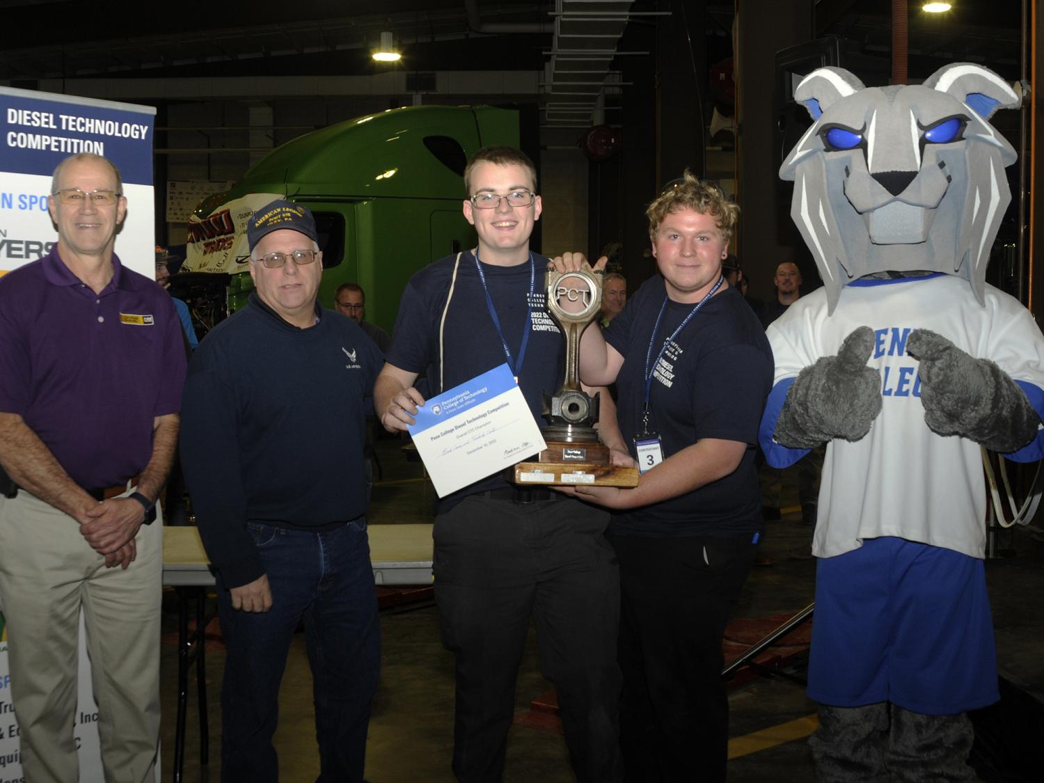 Five people and the Penn College Wildcat mascot pose with a trophy and a certificate