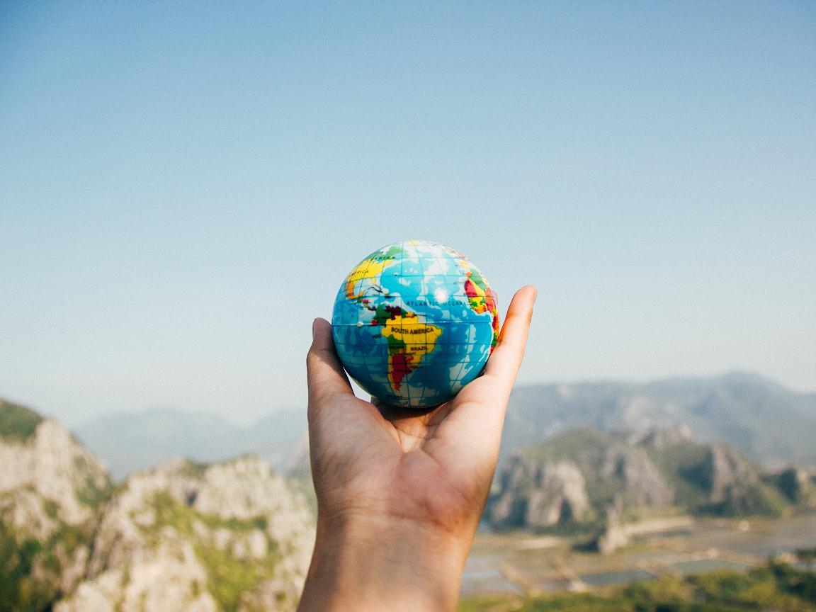 A hand holding a globe with mountains in the background