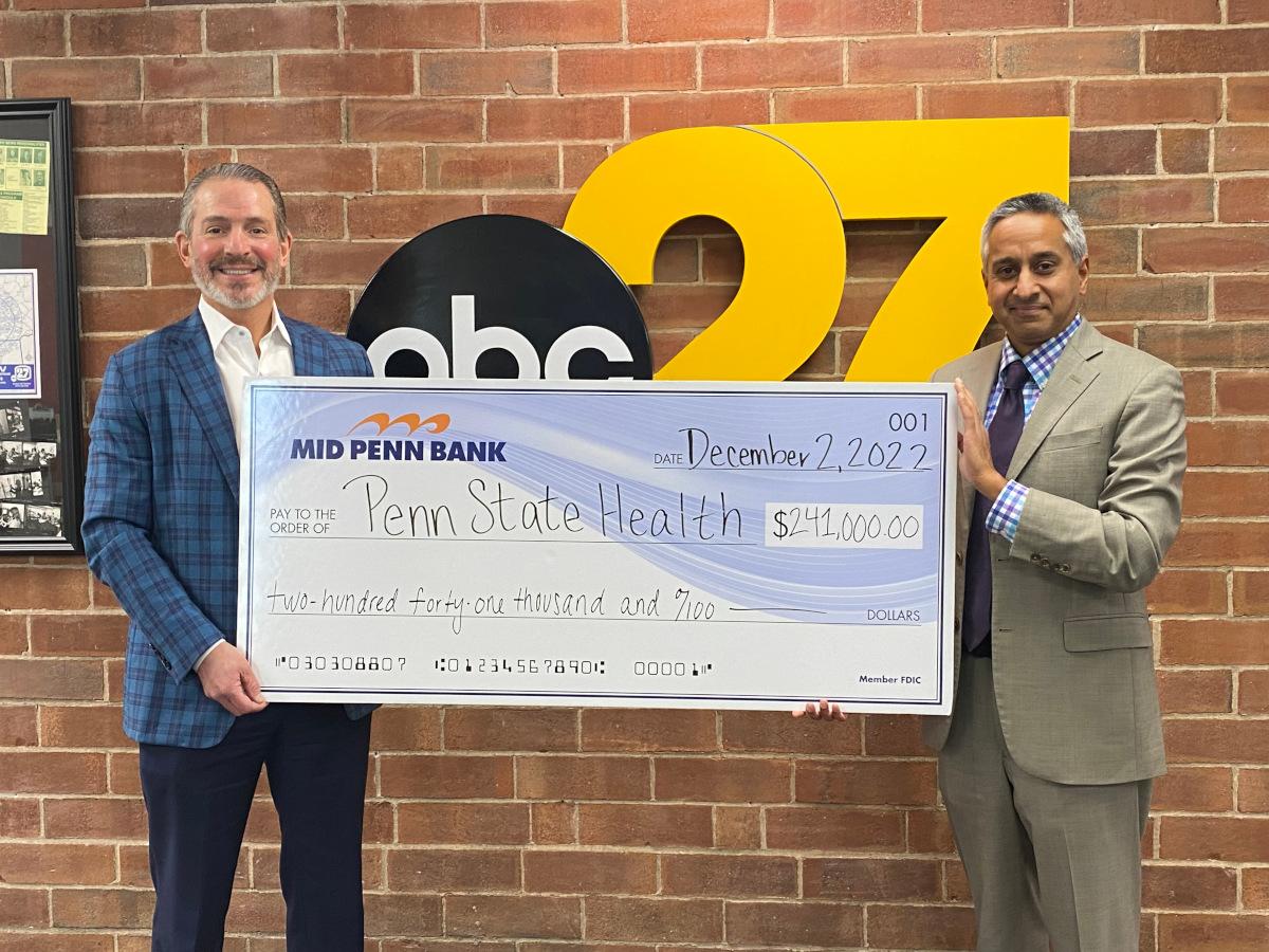 Two men are smiling and holding a big check for $241,000