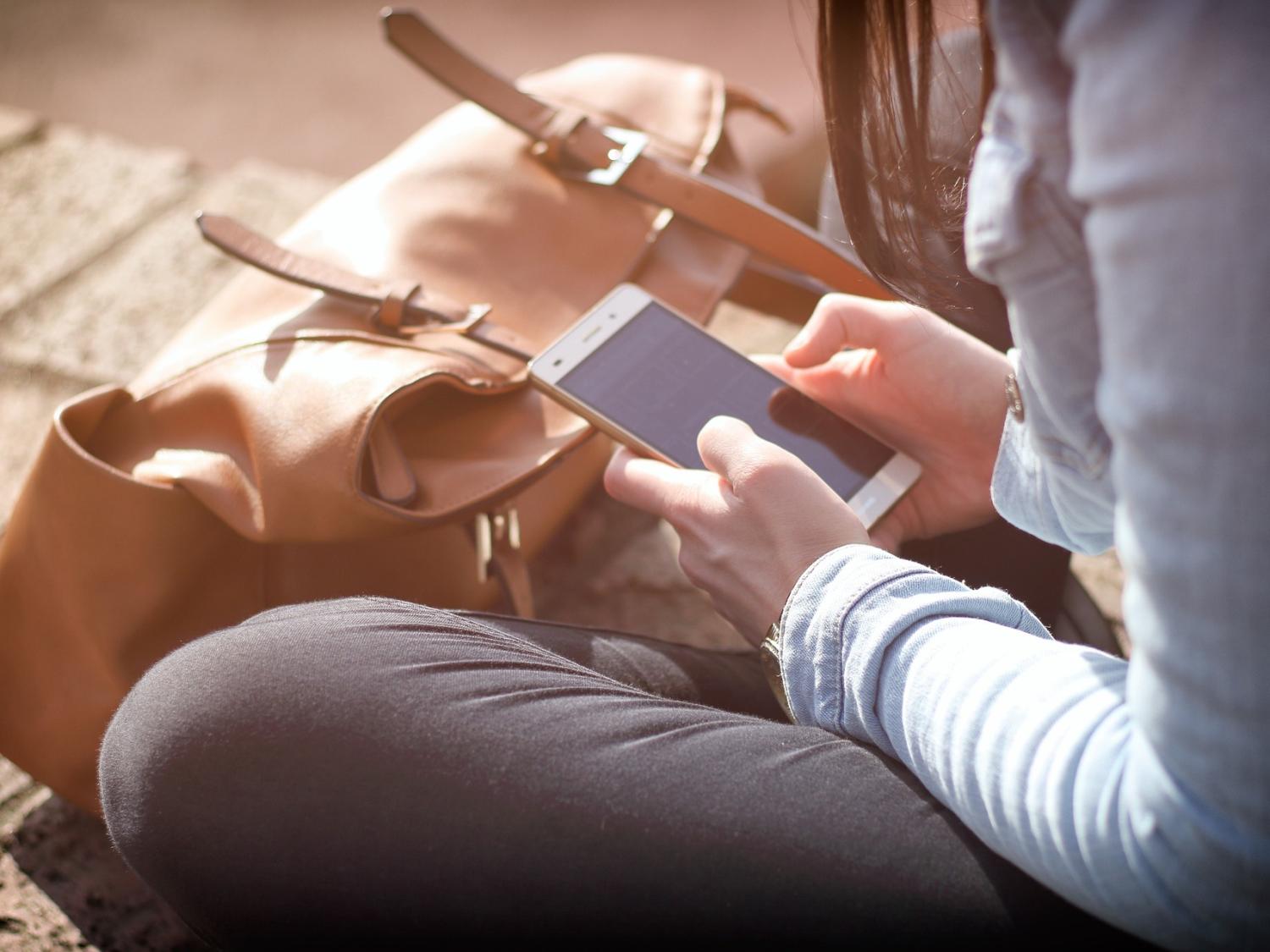 A woman sitting on the ground holding a smartphone