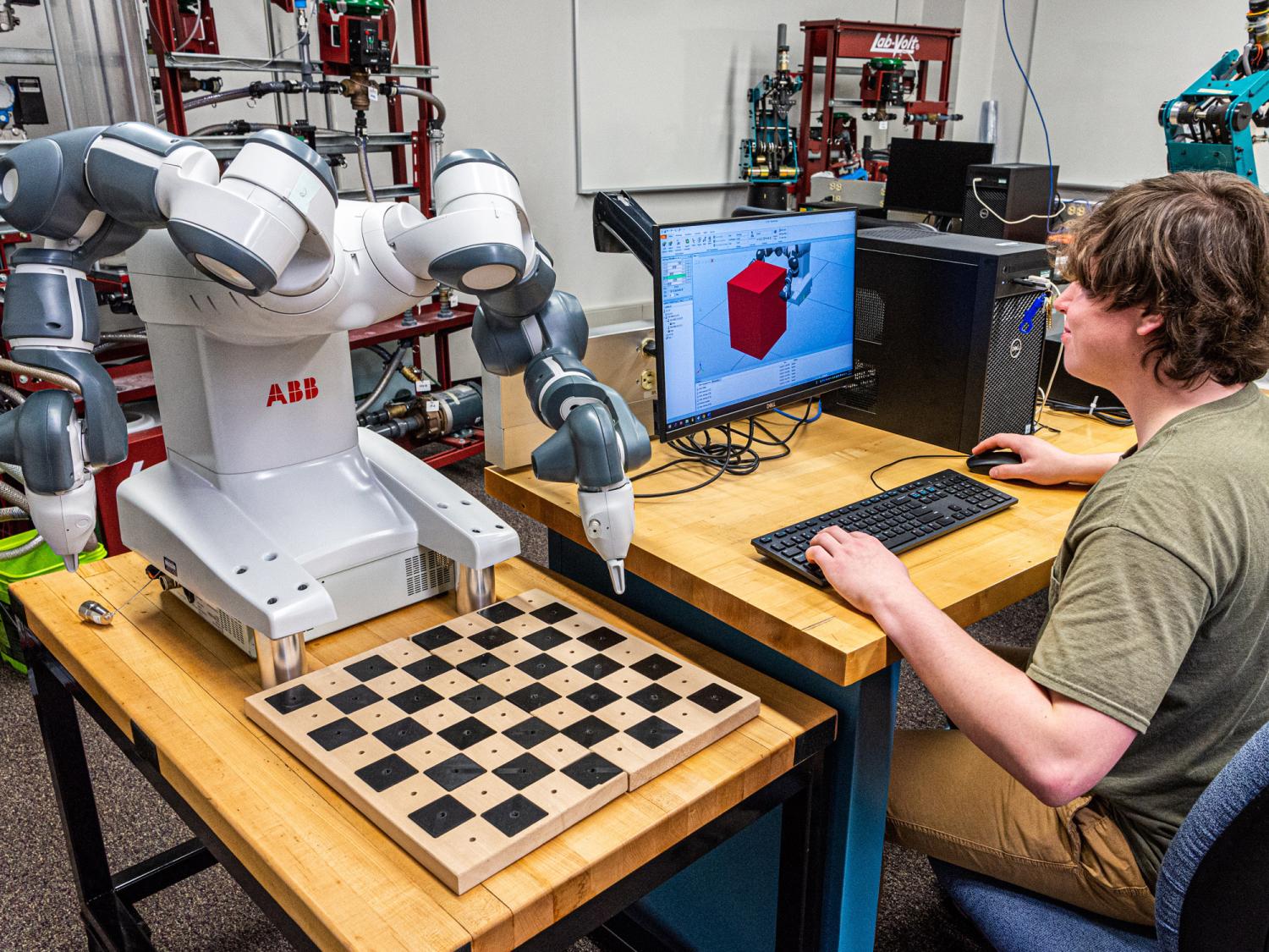 A student sitting at a computer with robotics equipment nearby